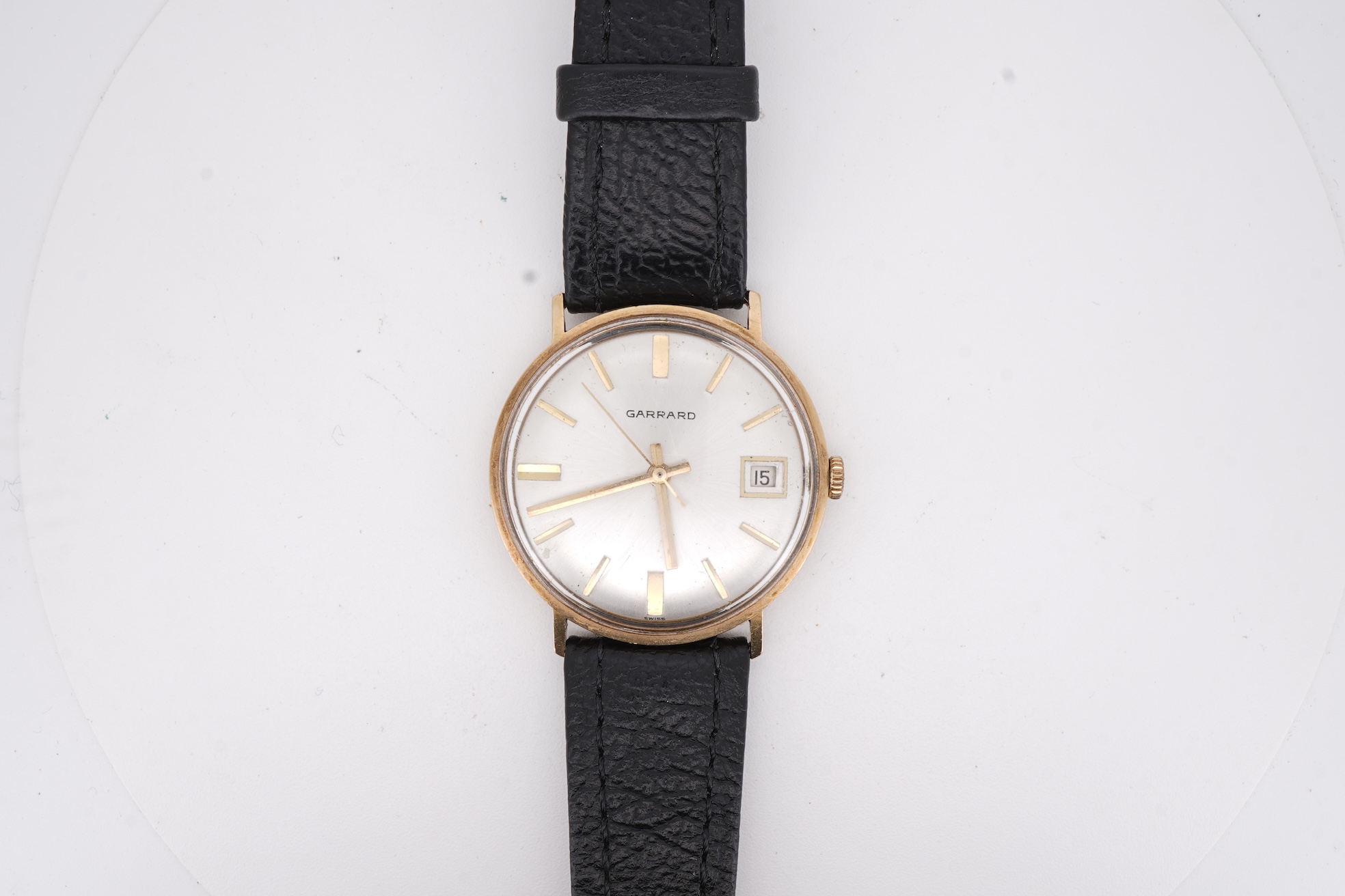 A gentleman's yellow metal Garrard manual wind wrist watch, with baton numerals and date aperture, case diameter 34mm, on a black leather strap.